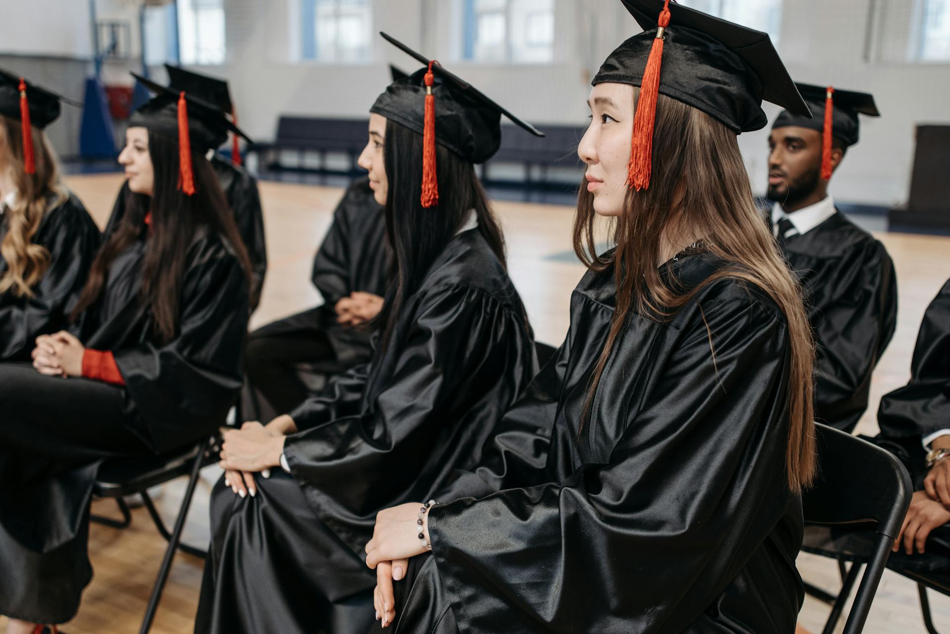 Graduates in caps and gowns seated indoors during a ceremony, celebrating academic success together.