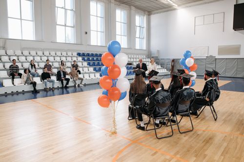 Free Graduation ceremony in a gymnasium with graduates in gowns and colorful balloons. Stock Photo