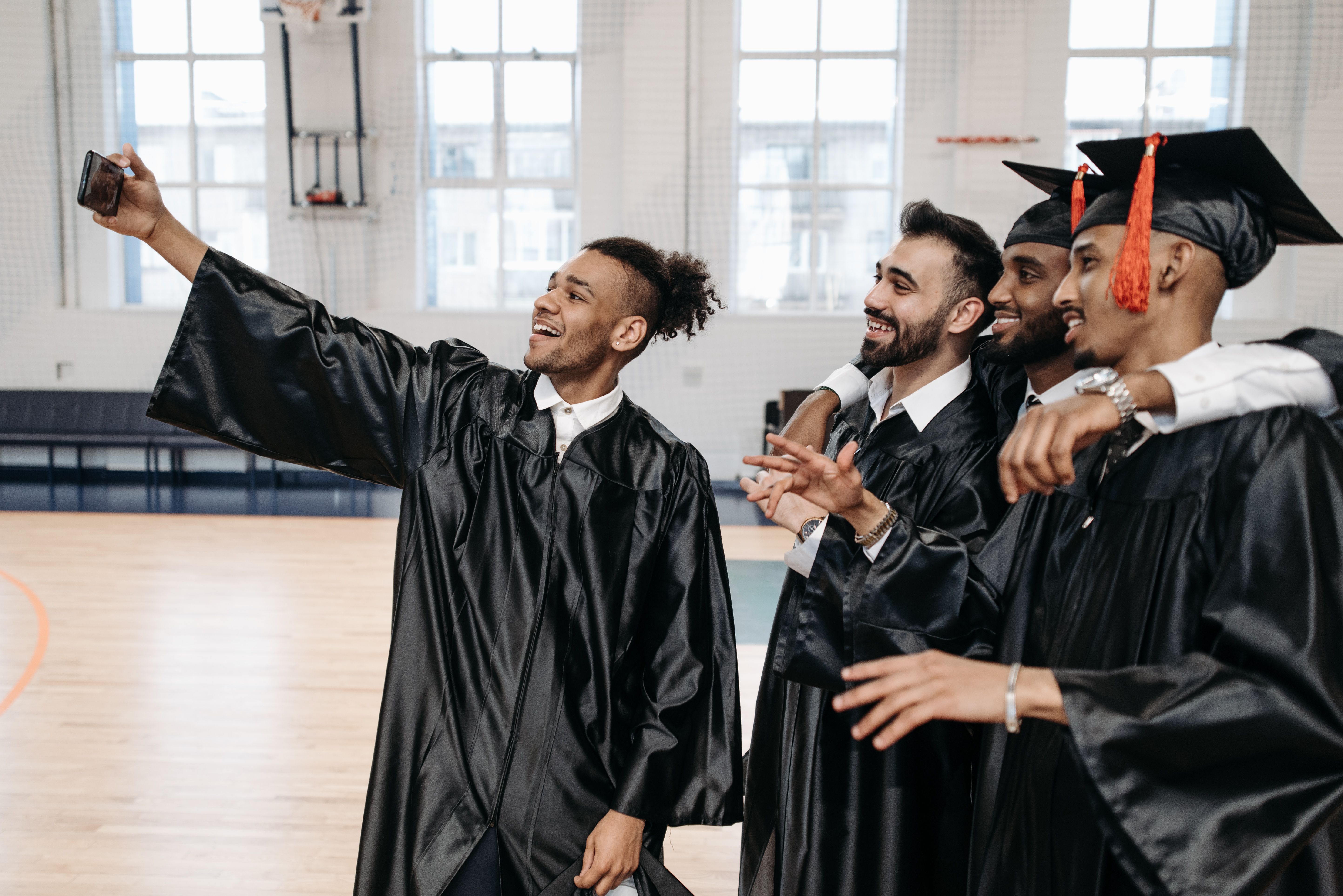 Joyful graduates in caps and gowns taking a selfie indoors, capturing a special moment.