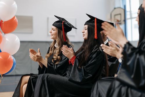 Free Graduates in caps and gowns applauding during a vibrant indoor ceremony celebrating success. Stock Photo