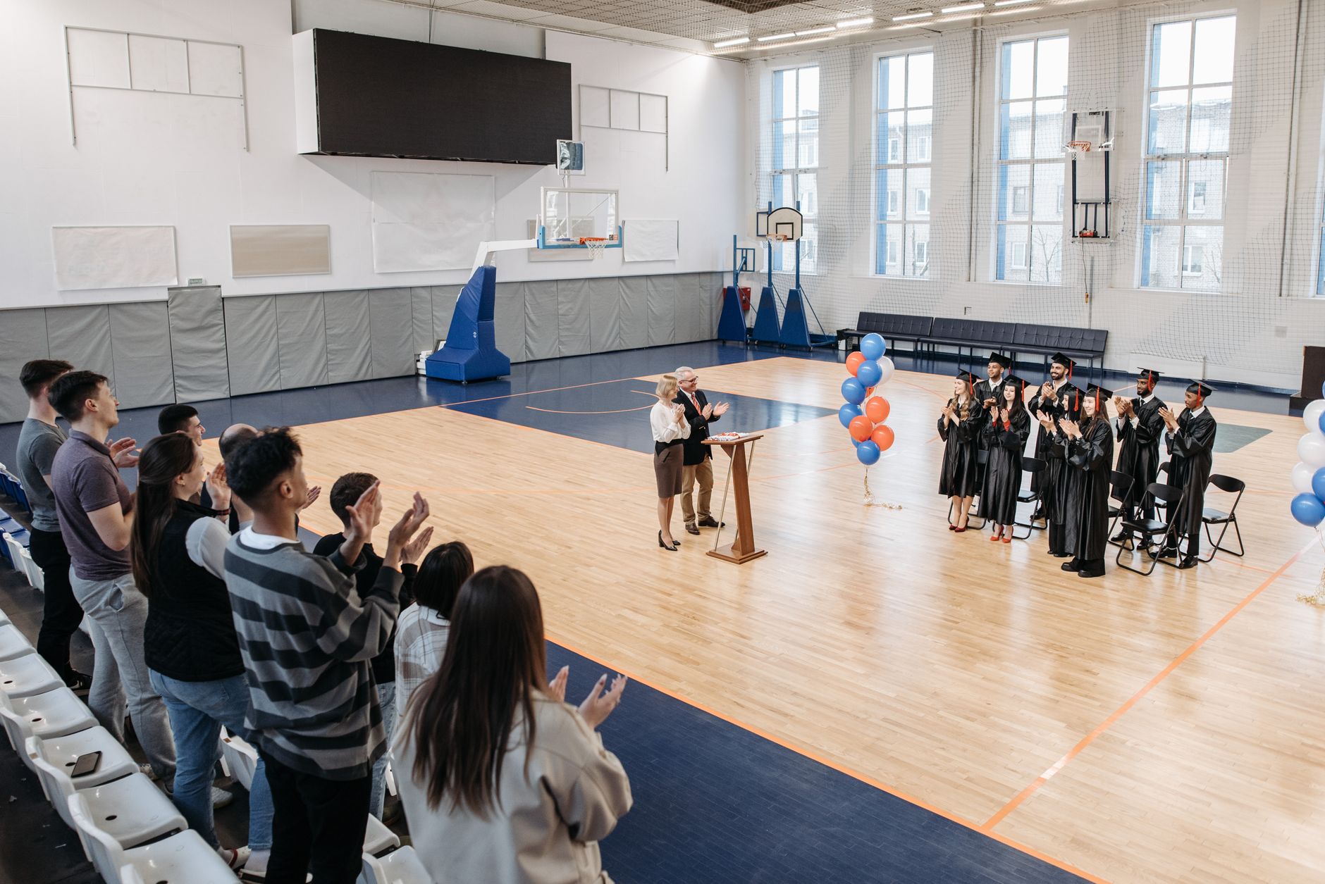 Graduates celebrate in an indoor gymnasium with friends and family during a graduation ceremony.