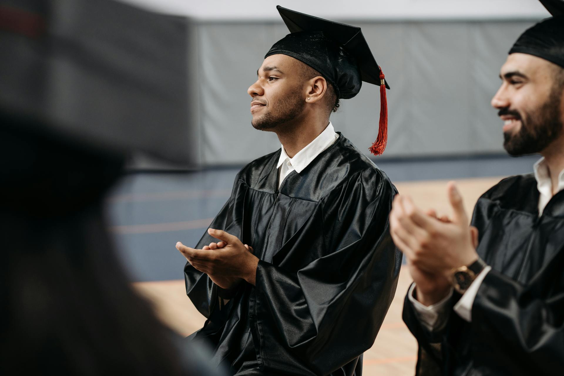 Graduates in caps and gowns applauding a special moment during a ceremony indoors.