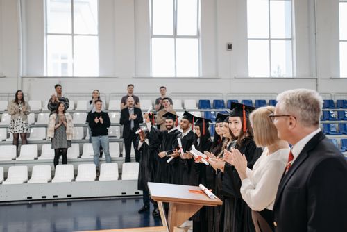 Free Graduates in gowns receive applause during an indoor ceremony, celebrating achievement. Stock Photo