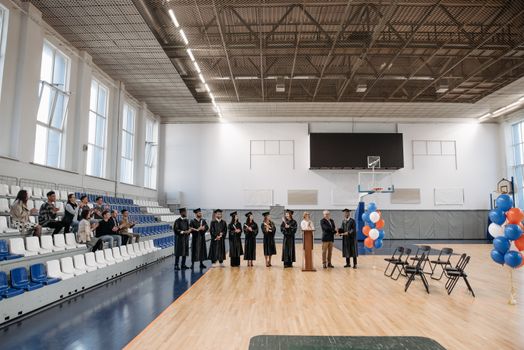 A graduation ceremony held in an indoor gymnasium with graduates and an audience.