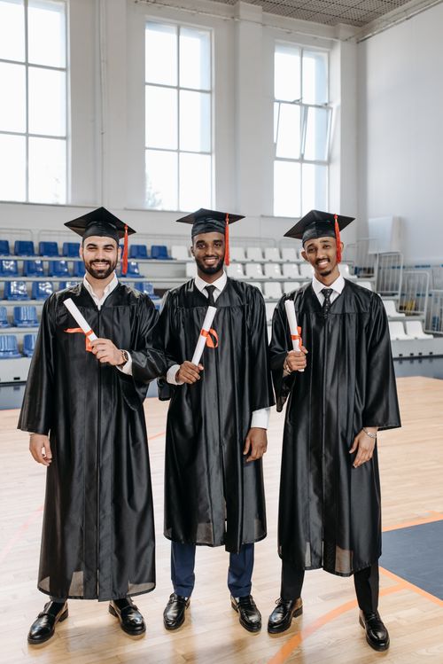 Free Three graduates in gowns holding diplomas, celebrating their achievement indoors. Stock Photo