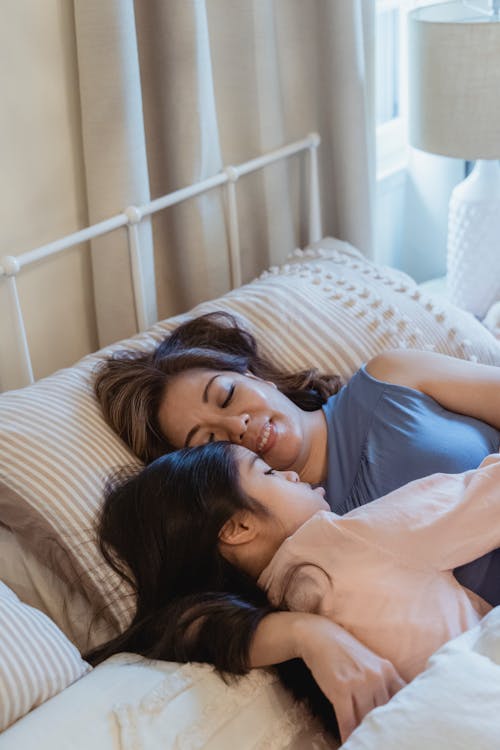 A Woman Embracing a Young Girl while Lying on the Bed