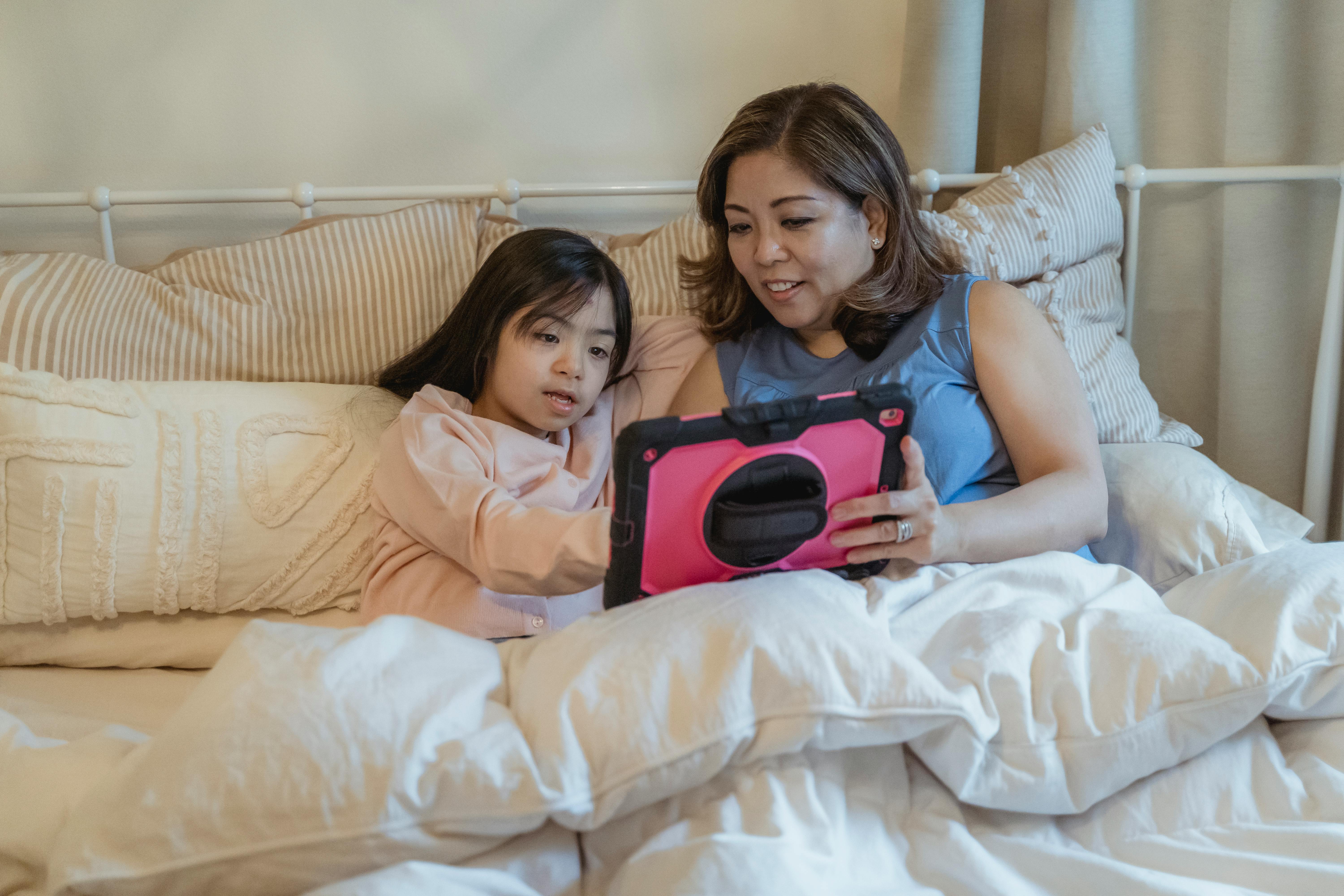 A cozy mother and daughter bonding time with a tablet in bed, showcasing family togetherness.