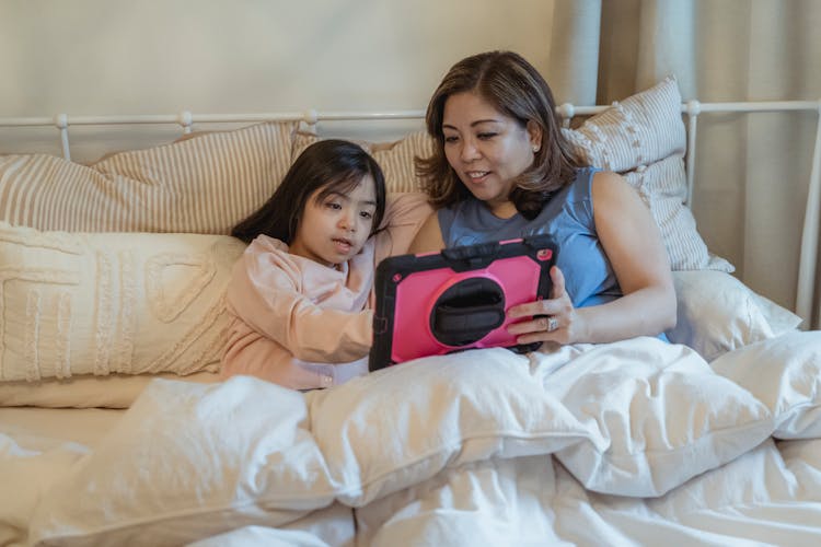 A Girl And A Woman On Bed Holding A Tablet