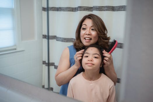 A mother gently brushes her daughter's hair in a cozy bathroom setting.
