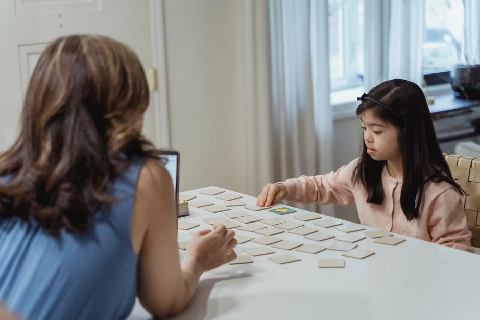 Ein junges Mädchen und ihre Mutter spielen an einem weißen Tisch ein Kartenspiel und verbringen so etwas Zeit mit der Familie.