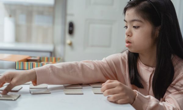 Special Needs Care — Young Asian girl with Down Syndrome engaged in a game indoors, wearing a pink sweater.
