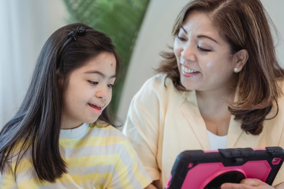 A mother and daughter bonding while using a tablet. Warm, joyful interaction.