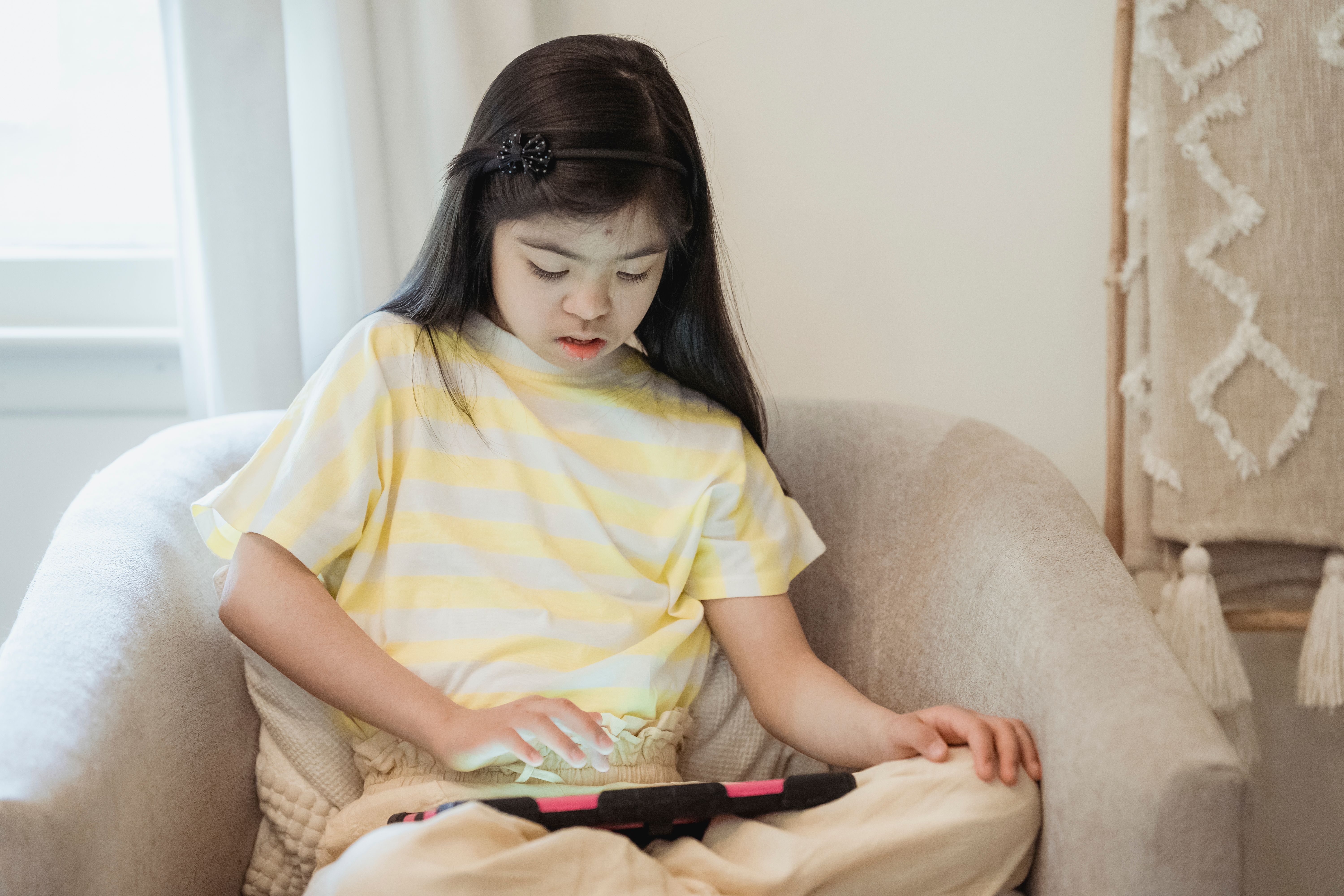 A Girl Using a Digital Tablet while Sitting on a Chair · Free Stock Photo