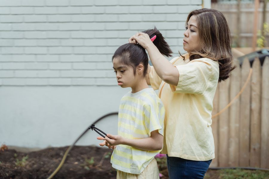 Mother gathering her daughter's long hair into a practical ponytail outdoors