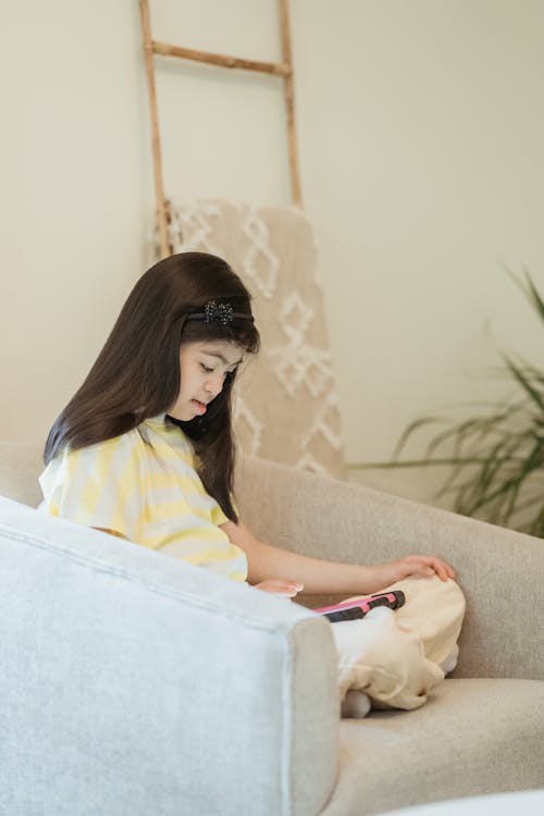 A Young Girl Sitting on the Sofa while Using Her Tablet