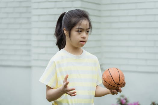 A young girl with Down syndrome holding a basketball outdoors.