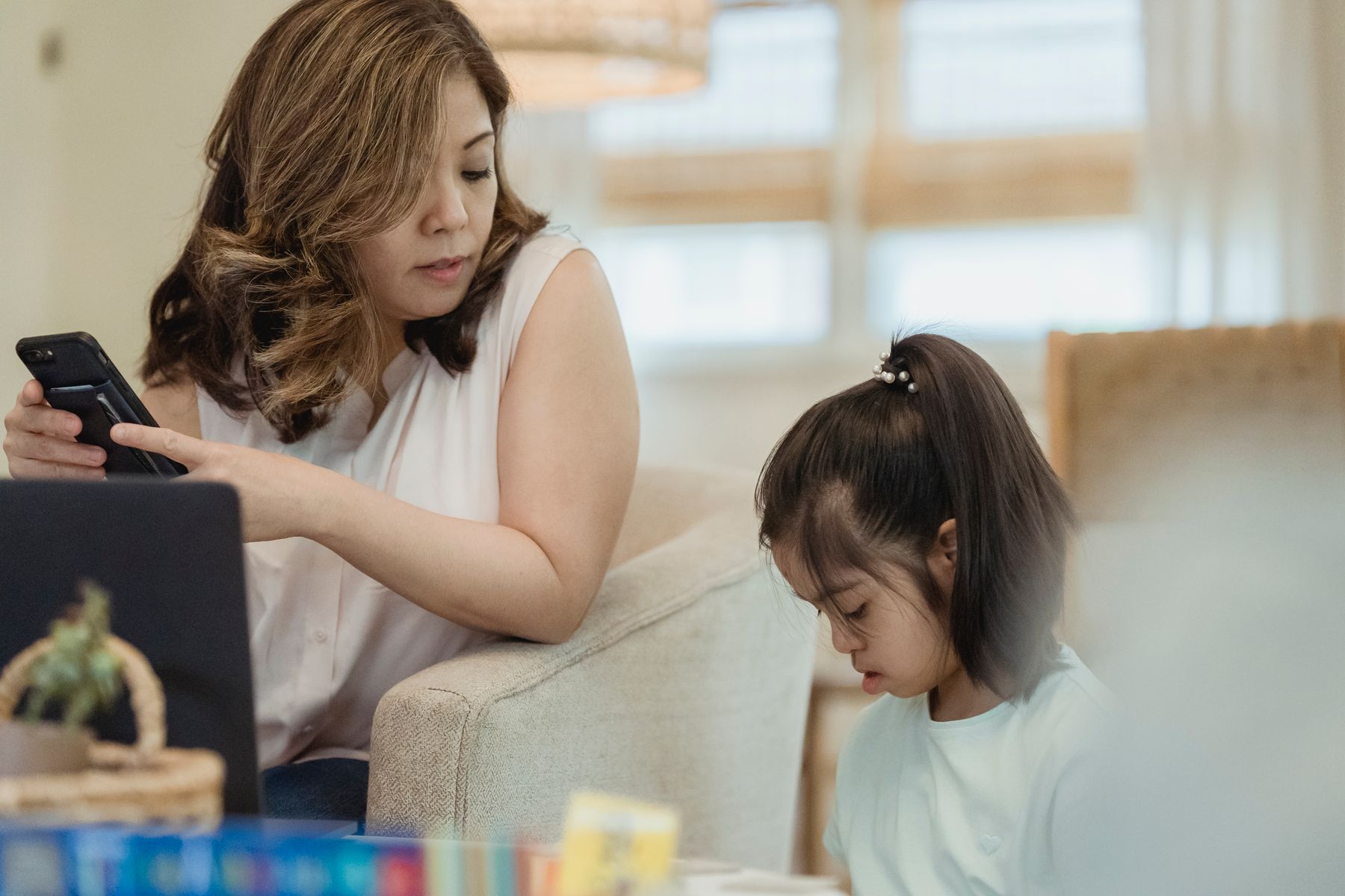 A mother checking a smartphone while spending time with her daughter