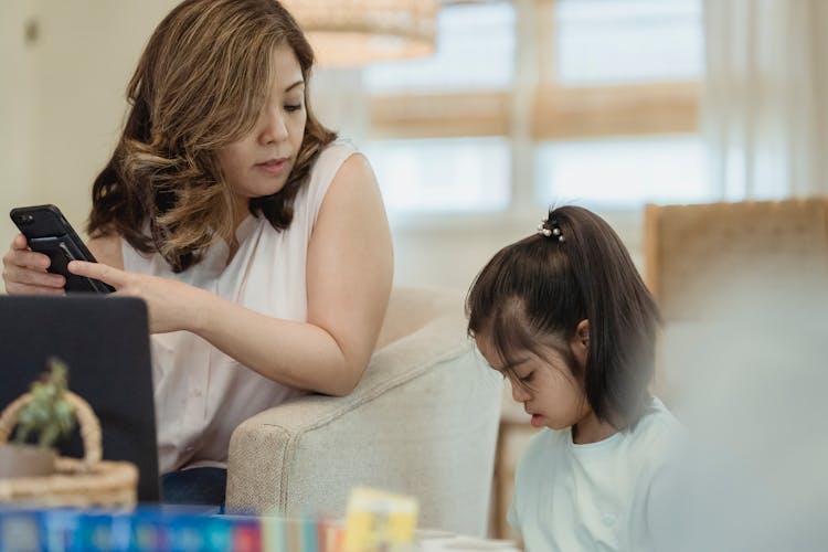 A Mother Holding Her Phone While Looking At Her Daughter