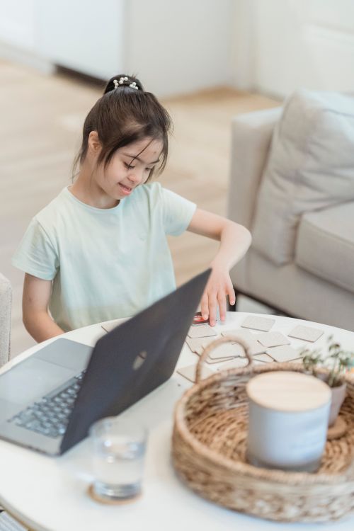 Free A cheerful girl focusing on educational materials beside a laptop in a comfortable indoor setting. Stock Photo