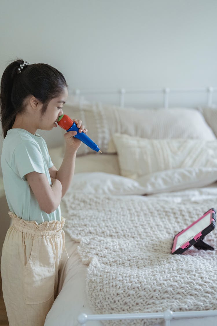 A Young Girl Standing Beside Her Bed While Singing