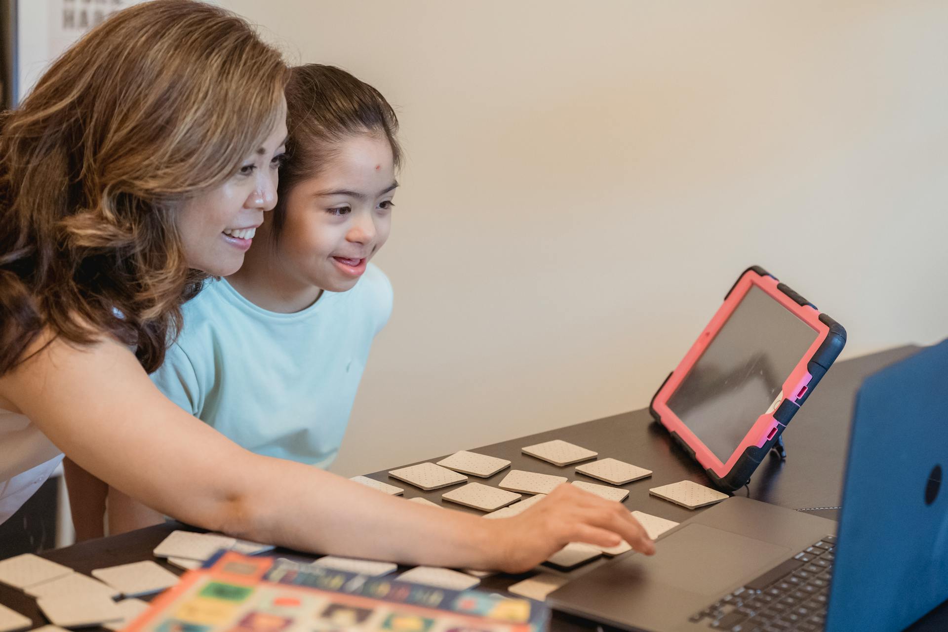 Asian mother and daughter enjoying learning together with a laptop and educational cards indoors.