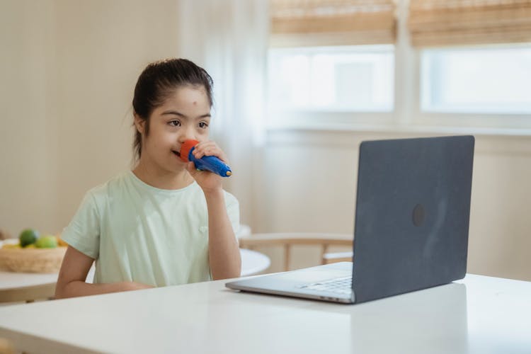 A Young Girl In White Shirt Singing While Looking At Laptop