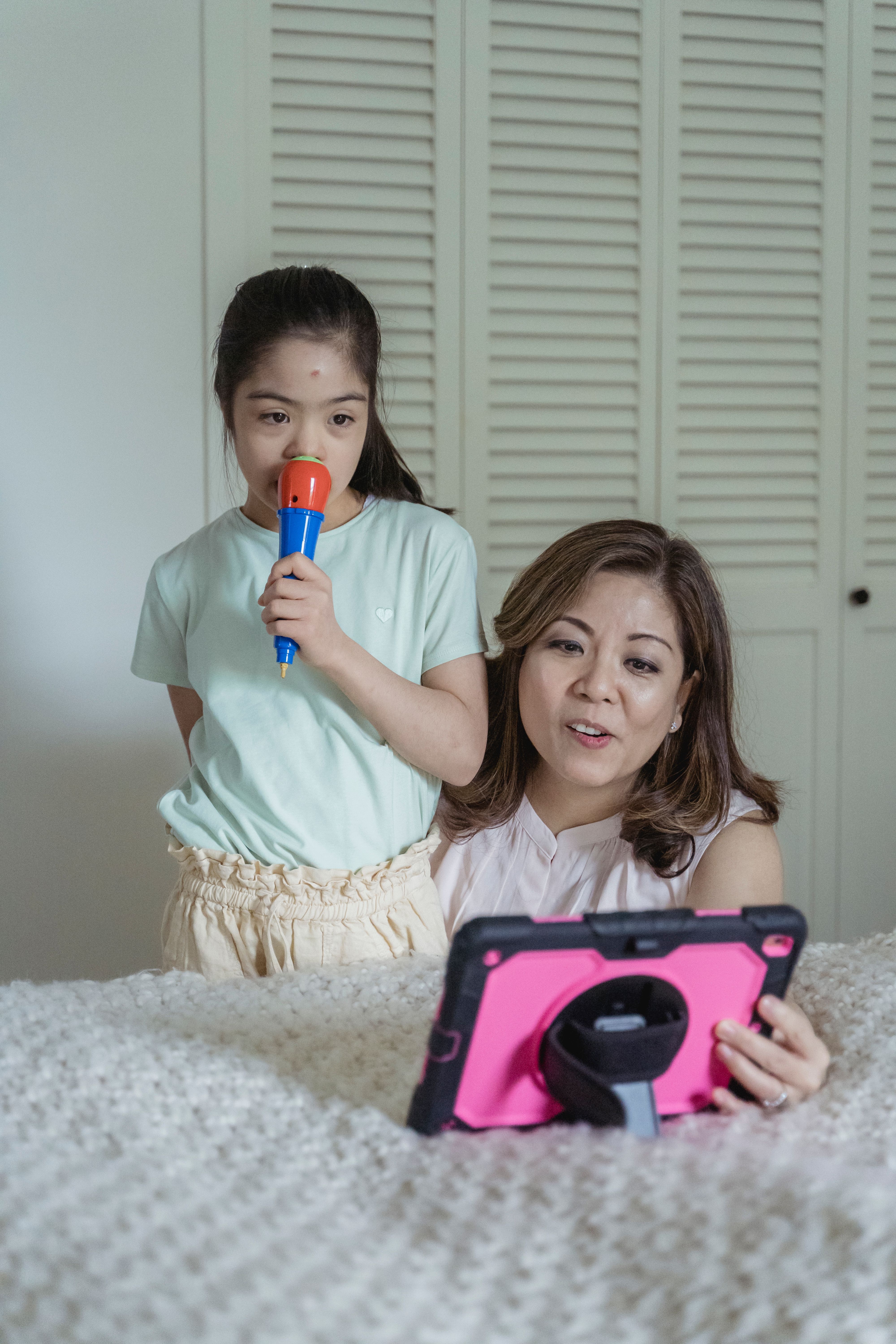 Mother and daughter enjoying leisure time with a tablet and microphone indoors.