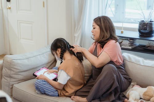 Free A Woman Braiding Her Daughter's Hair while Sitting on the Couch Stock Photo