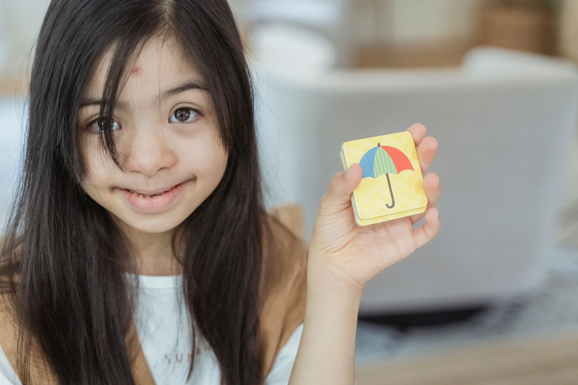 Young girl indoors smiling and showing a card with an umbrella image.