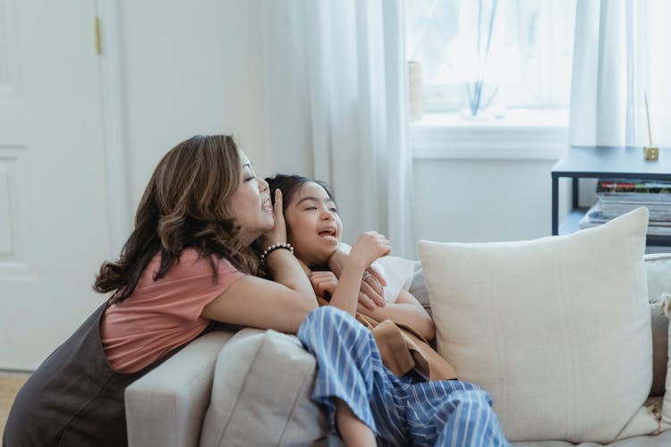 A Mother And Her Daughter Laughing Together Near A Throw Pillow