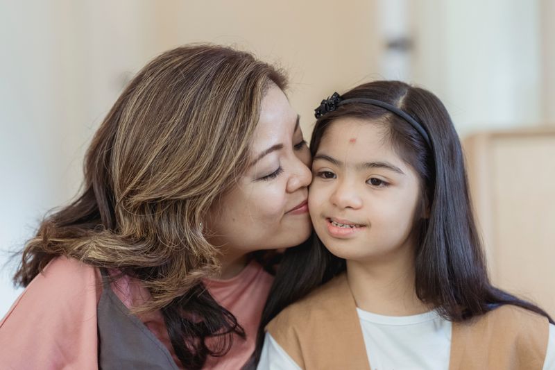 Heartwarming moment of a mother lovingly kissing her daughter with Down syndrome.