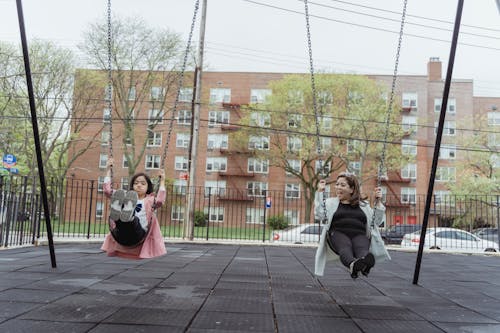 Free Mother and Daughter Sitting on Swings in a Public Playground Stock Photo
