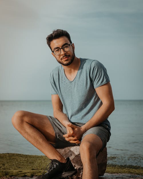 Free A Man in Blue Shirt Sitting on the Shore Stock Photo
