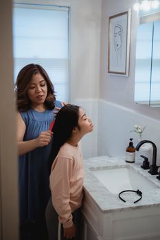 Mother helps daughter brush hair in cozy bathroom setting.
