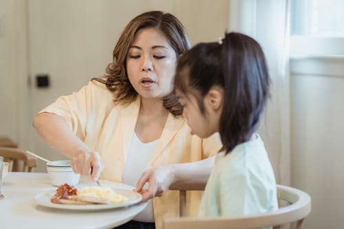 Mom Feeding Her Daughter with Breakfast
