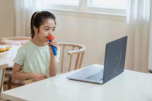 Free Young girl singing into a toy microphone, enjoying playtime with a laptop indoors. Stock Photo