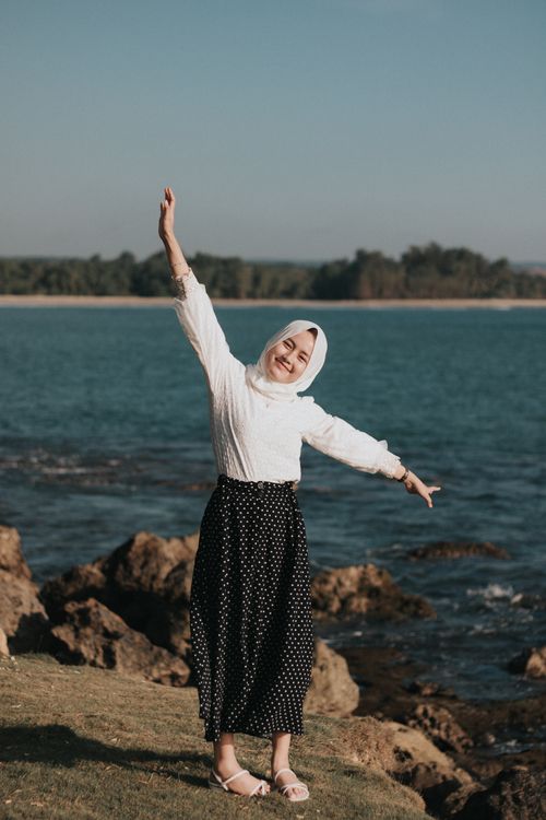 Free Smiling woman in headscarf enjoying a sunny day by the sea. Vibrant and joyful moment. Stock Photo