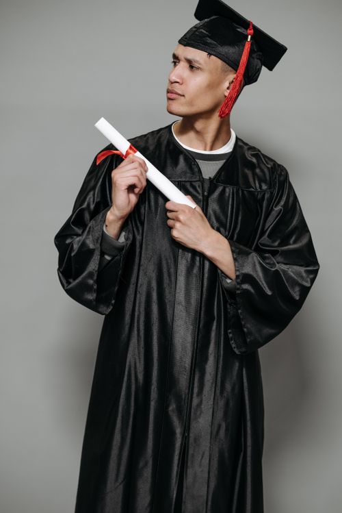 Free A proud graduate in cap and gown holds a diploma, symbolizing academic achievement and success. Stock Photo