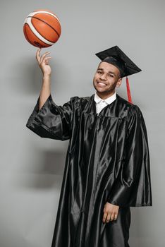 Graduate wearing gown and mortarboard spinning a basketball, symbolizing achievement and balance.