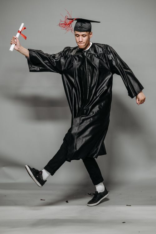 Free Happy graduate in cap and gown joyfully dancing with diploma. Stock Photo