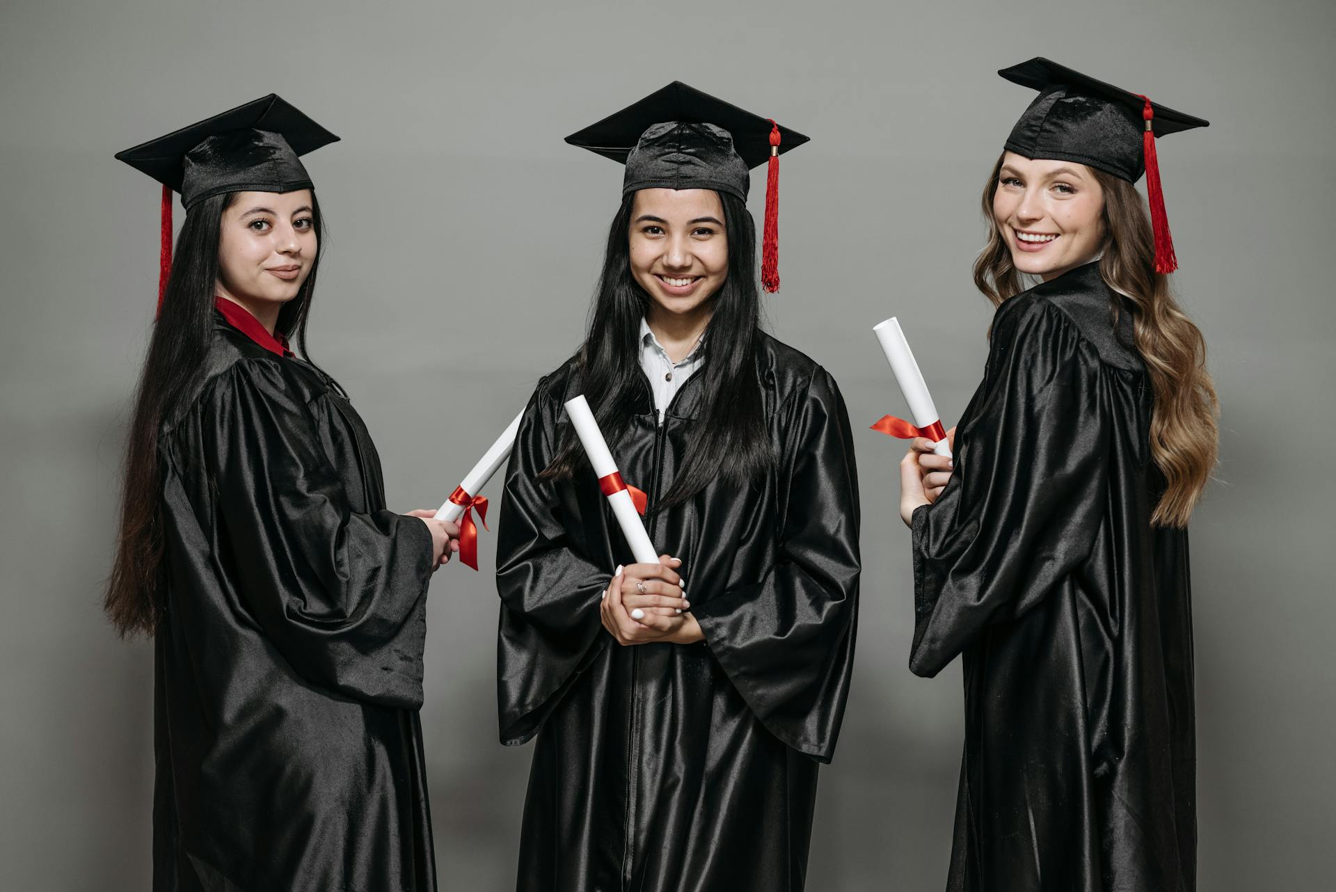 Three diverse women in graduation gowns celebrating achievement with diplomas.
