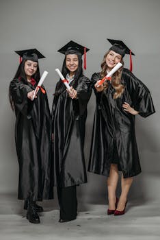 Three women in graduation gowns celebrating with diplomas, smiling proudly.