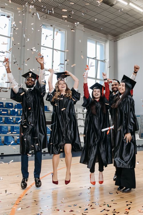Free Graduates in gowns rejoice with confetti inside a gymnasium, celebrating success and achievement. Stock Photo