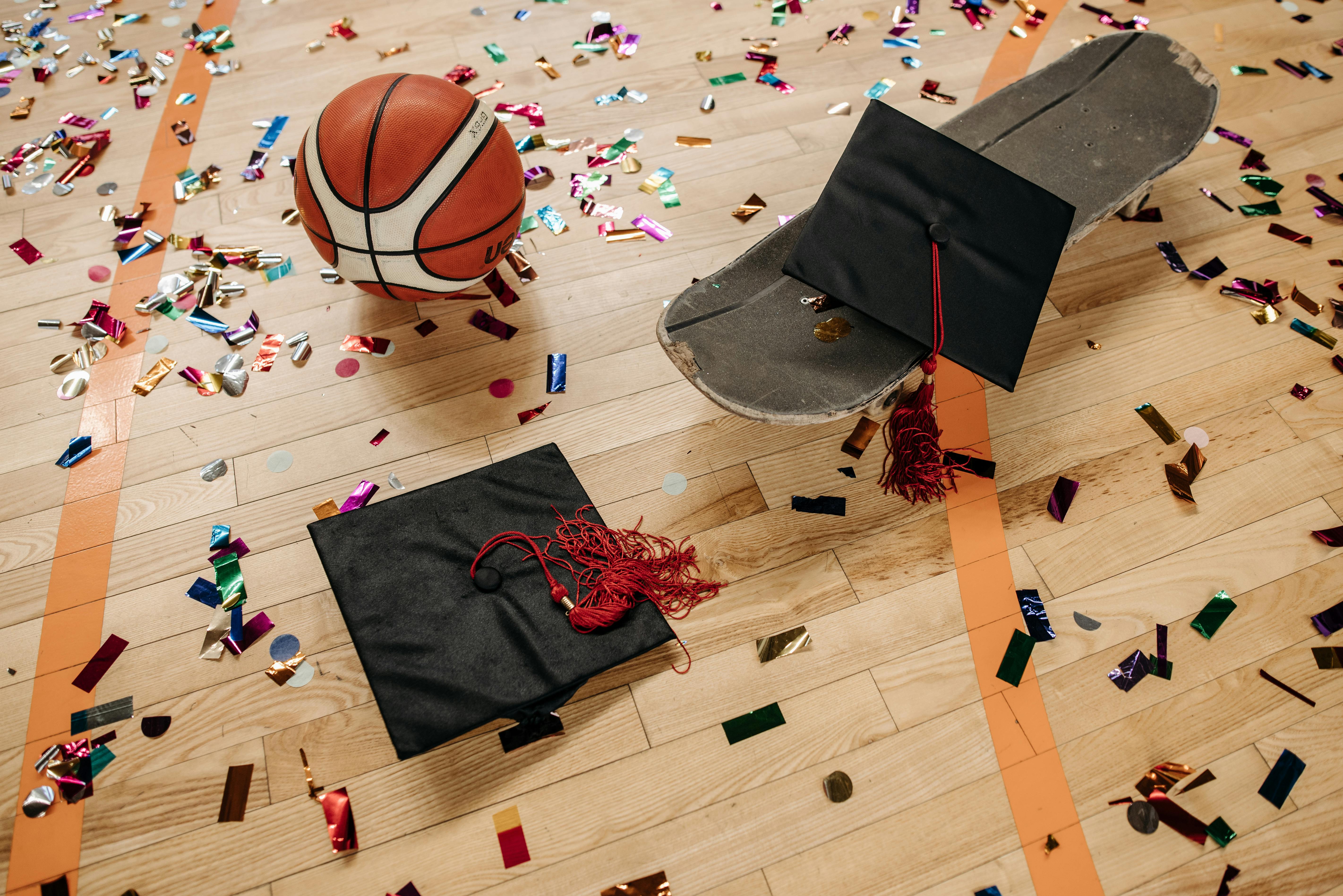 Free Graduation caps and basketball on confetti-covered court with skateboard, a unique blend of celebration and sports. Stock Photo