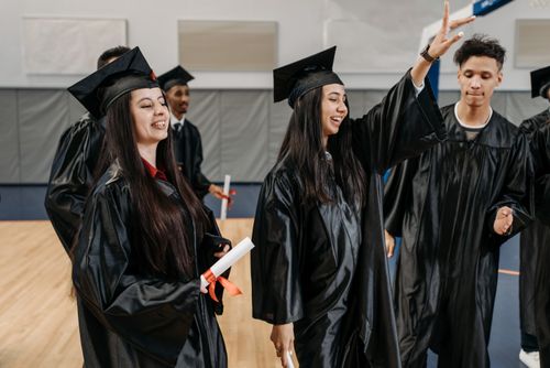 Free Group of graduates celebrating in caps and gowns indoors, expressing happiness and achievement. Stock Photo