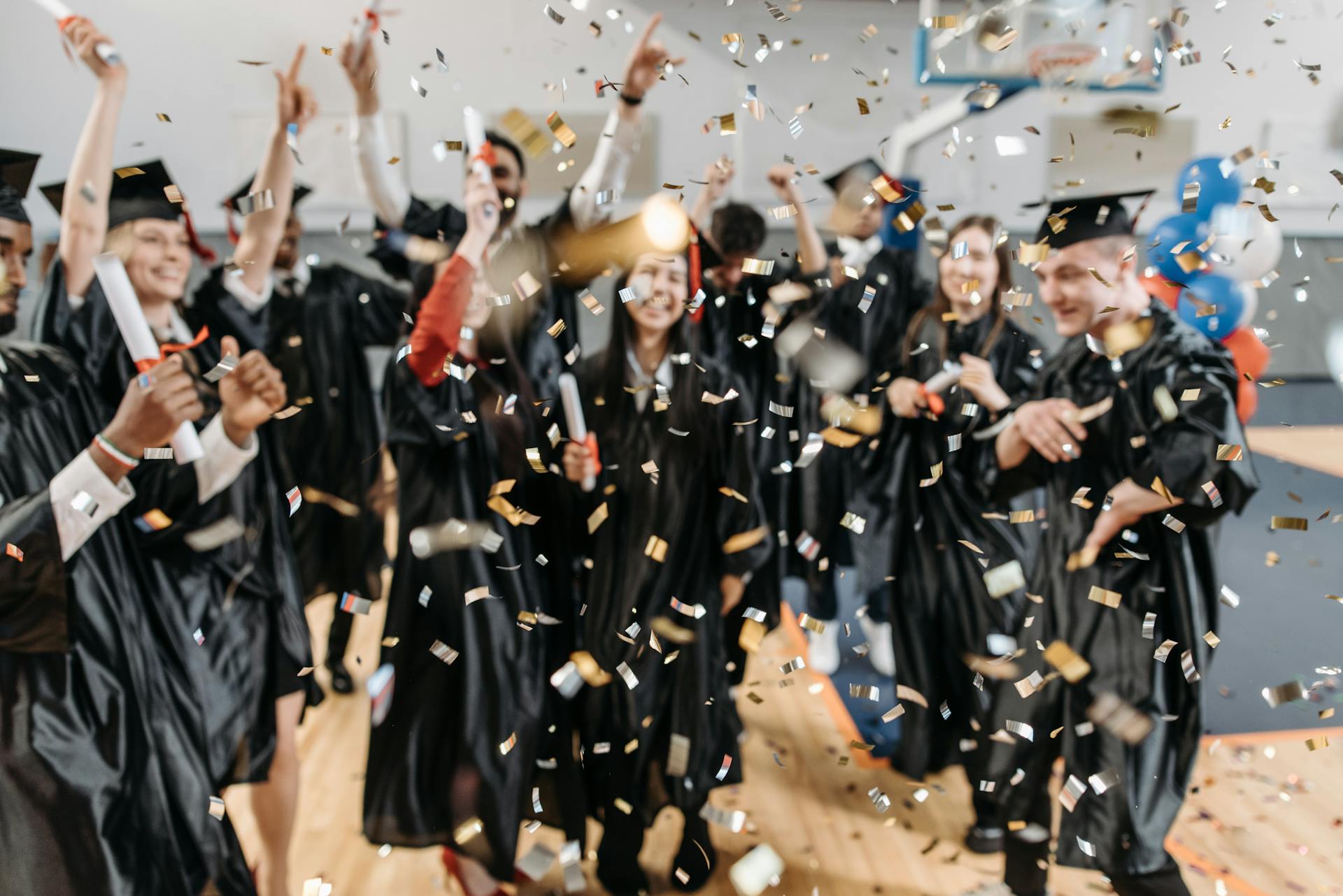 Excited graduates toss confetti in celebration, marking a special achievement moment indoors.