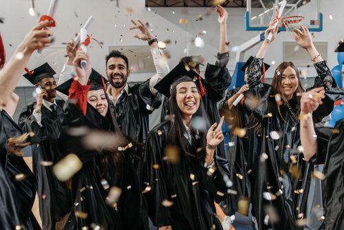 Free Group of diverse students celebrating graduation with confetti indoors. Stock Photo