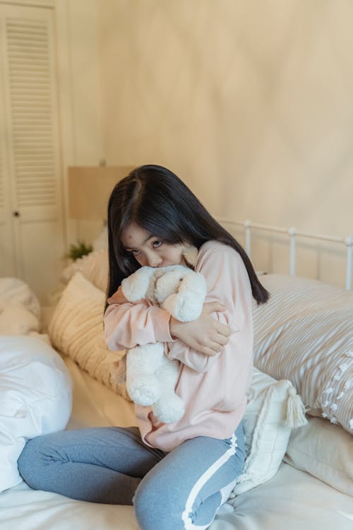 A Young Girl Sitting on Her Bed while Hugging Her Stuffed Toy