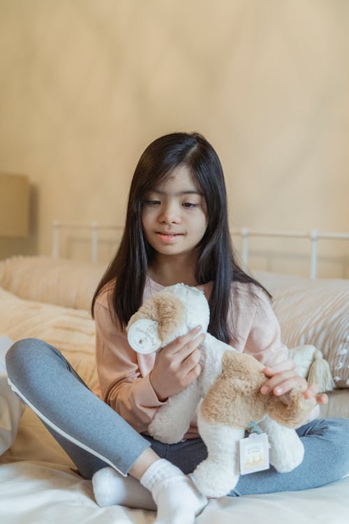 A Young Girl Sitting on the Bed while Holding Her Stuffed Toy