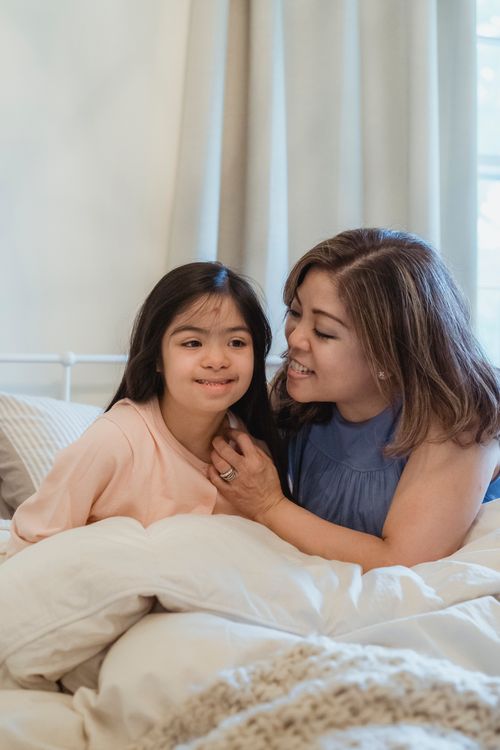Free A heartwarming scene of a mother bonding with her daughter, both smiling in a cozy indoor setting. Stock Photo